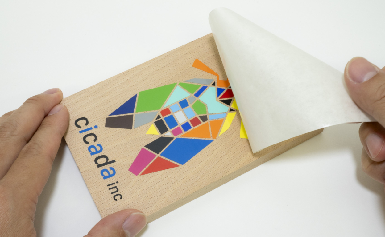 15色仕様で作られた蝉のデザインのカッティングシートを木材に貼っている