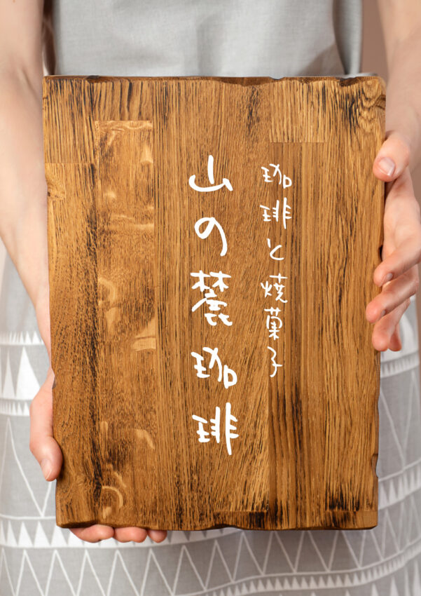 カッティングシートが貼られた木製看板を女性が手に持っている写真